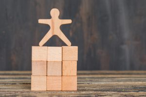 Business success concept with human model on wooden cubes on wooden background side view.